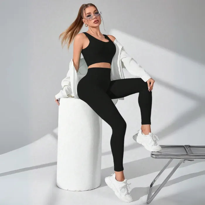 Athletic two-piece set in black ribbed fabric with white leg warmers and chunky sneakers, studio photography with dramatic shadows