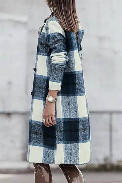 Back view of a woman wearing a blue and white plaid wool coat styled with brown leather pants in an outdoor urban setting.