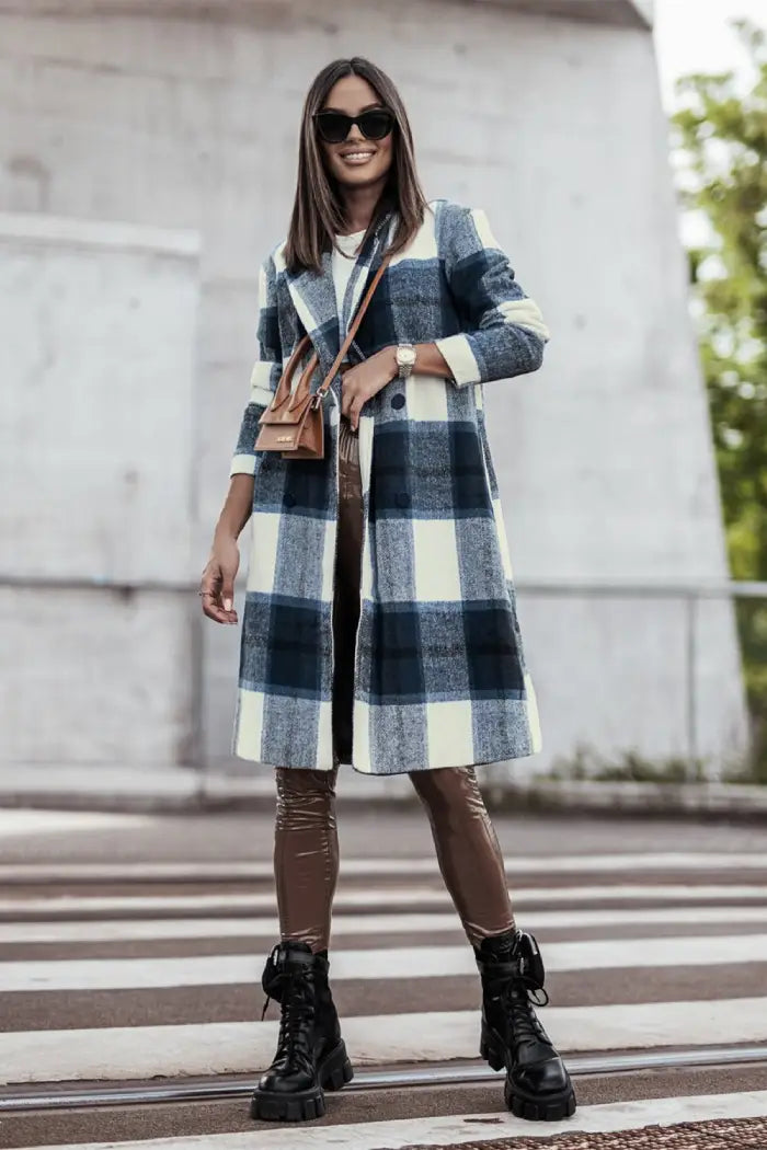 Full-length view of a woman in a blue and white plaid wool coat paired with brown leather pants, black boots, and a tan handbag outdoors.