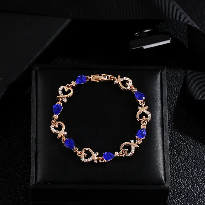 Blue gemstone gold bracelet in a black gift box, featuring elegant heart designs and sparkling accents.