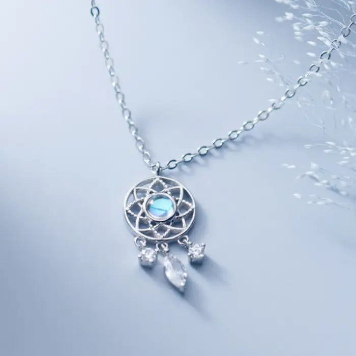 Blue luminous dreamcatcher necklace with crystal charms displayed on a light blue surface with delicate accents.