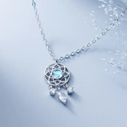 Blue luminous dreamcatcher necklace with crystal charms displayed on a light blue surface with delicate accents.