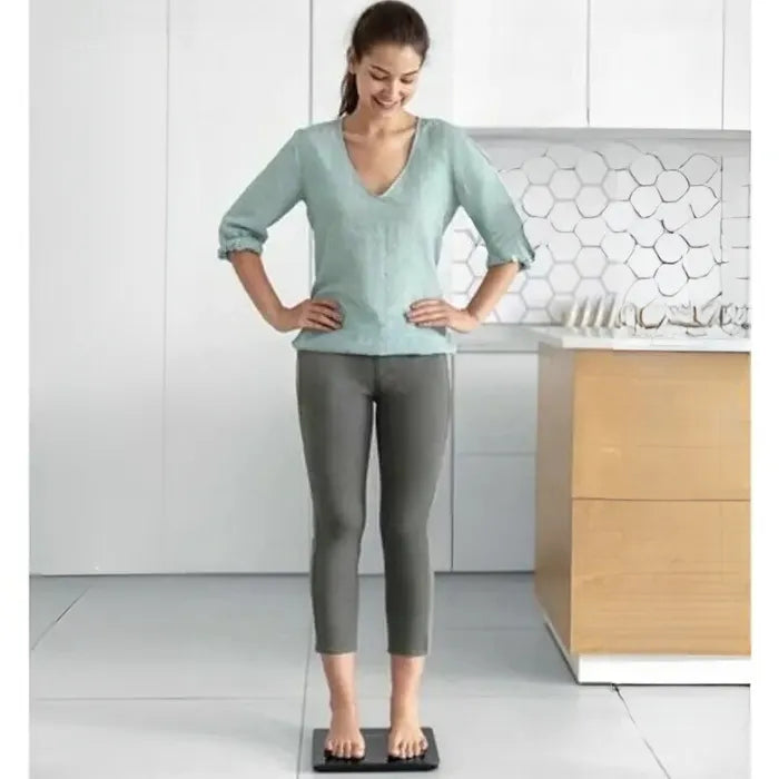 Woman standing on smart scale displaying body composition metrics including weight, BMI, body fat, and muscle mass analysis