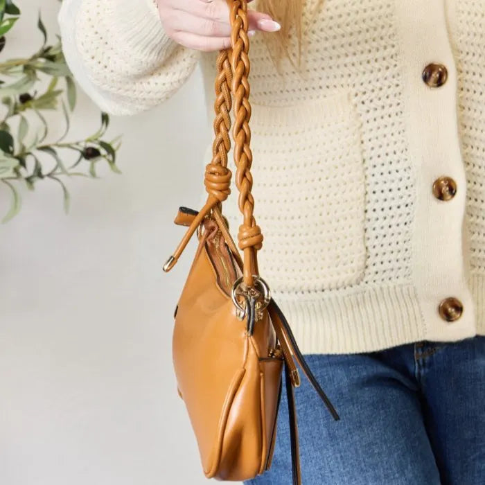 Detailed view of tan leather handbag's intricately braided handle with decorative tassels and silver hardware attachments