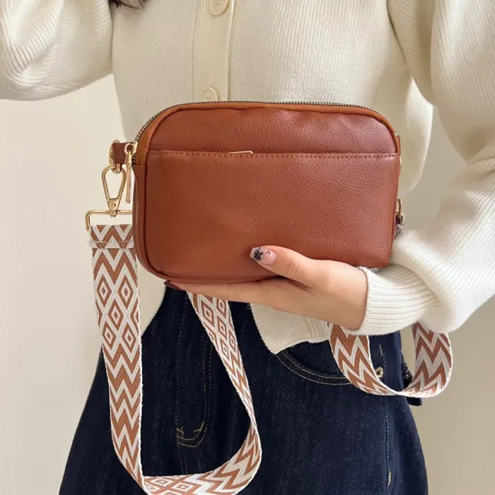 Brown crossbody bag with a patterned strap featuring diamond shapes, ideal for casual and stylish outfits.