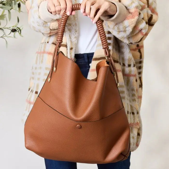 Brown leather handbag with coiled handle held by woman in plaid coat