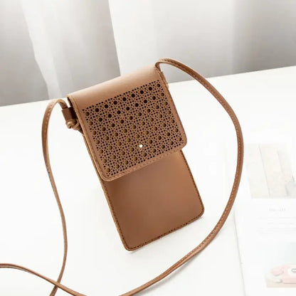 Brown leather crossbody phone bag with intricate perforated flap design, displayed on a clean table surface.