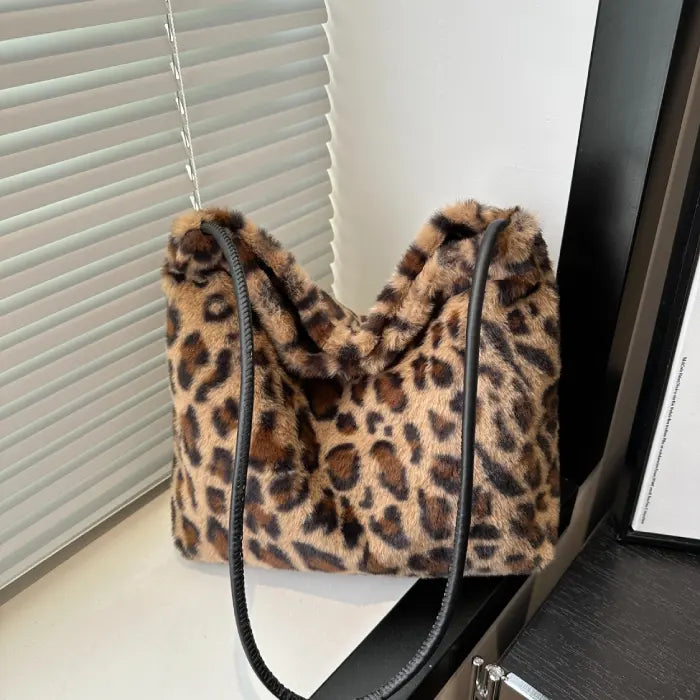 Brown leopard print faux fur handbag with a black strap placed near a window for stylish display.