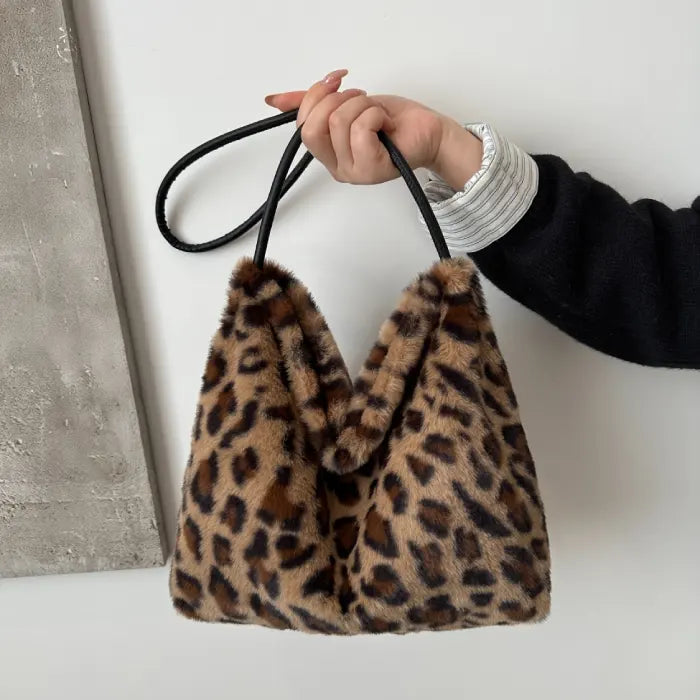 Hand holding a brown leopard print faux fur handbag with slim black strap for an elegant style.