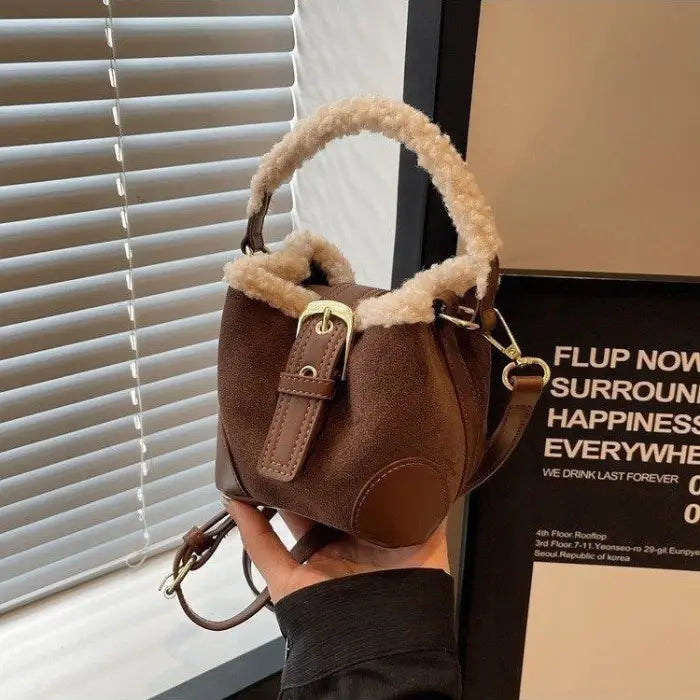 Brown suede mini bucket bag with sherpa-trimmed handle displayed against window blinds with motivational text