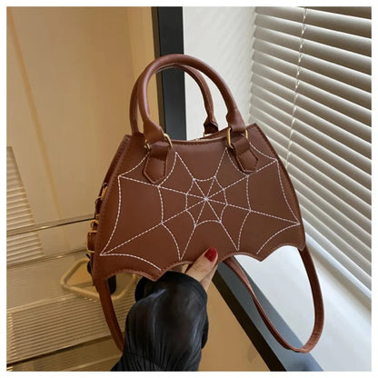 Brown leather handbag with white spiderweb stitching, bat-wing shape, held by hand with red nails near white blinds