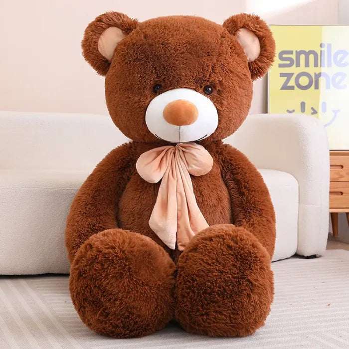 Large white teddy bear with maroon bow, sitting against a sofa.