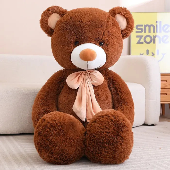 Large white teddy bear with maroon bow, sitting against a sofa.