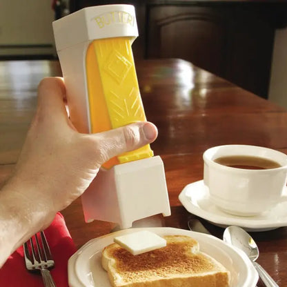 Hand pressing a butter dispenser to spread a square pat of butter on toast, with coffee on a wooden table.