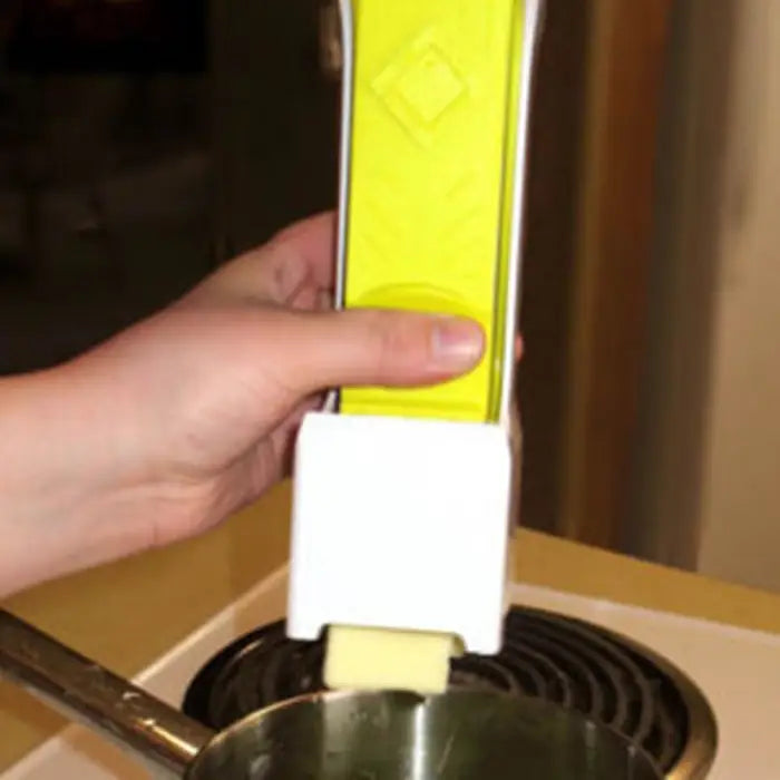 Hand using a yellow and white butter dispenser to spread butter onto a pan on a stovetop.