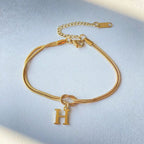 Gold bracelet with a 'H' charm on a light blue background
