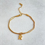 Gold bracelet with a 'R' charm on a light gray background