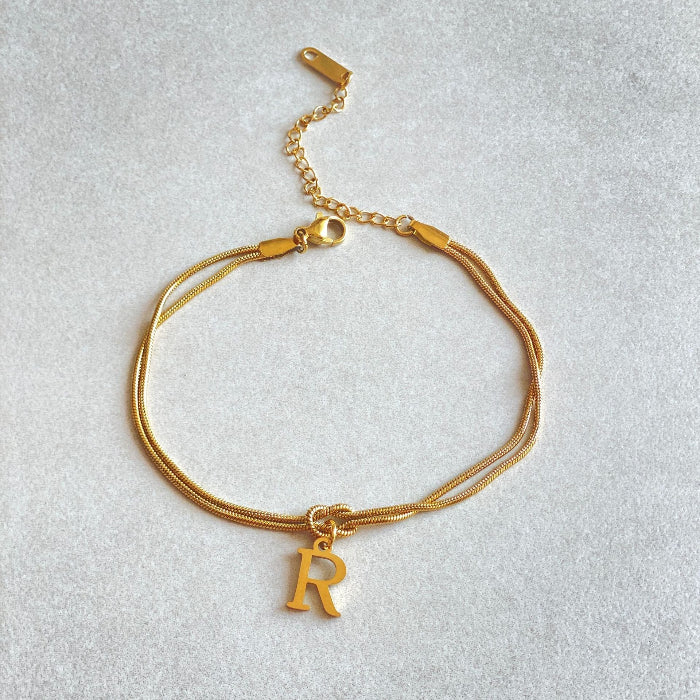 Gold bracelet with a 'R' charm on a light gray background