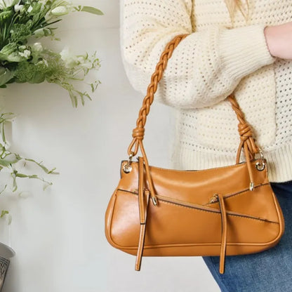 Camel brown leather shoulder bag with distinctive braided handle and silver hardware shown against cream knit cardigan