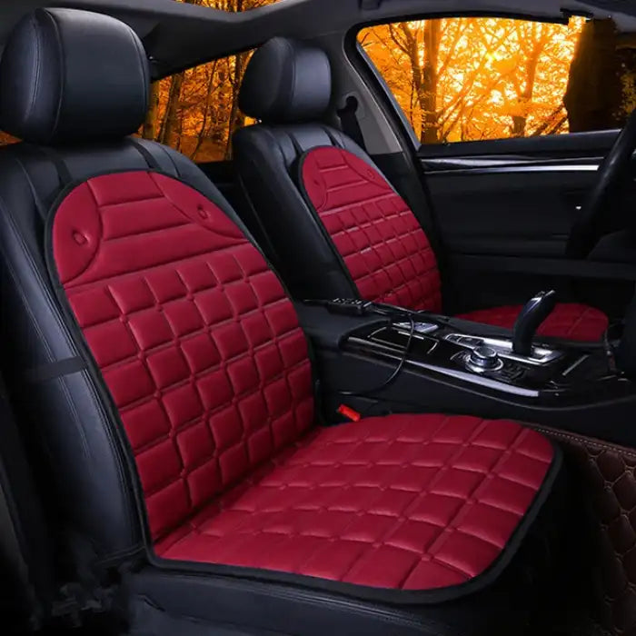 Car Seat Heater red quilted pads on both front seats in dark interior with orange forest view.