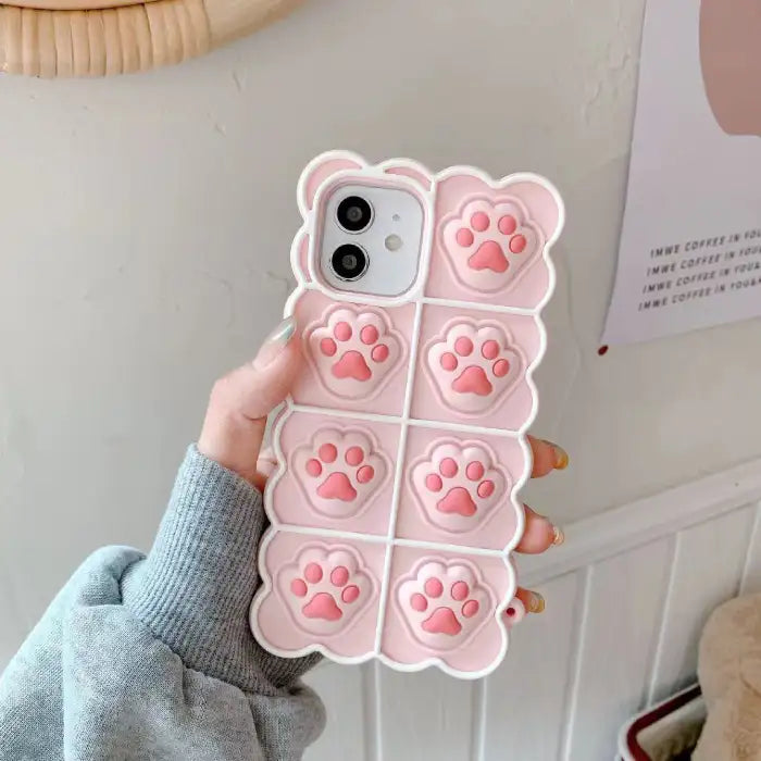 Cat paw phone case in soft pink silicone with 3D raised paw prints featuring detailed toe beans and protective iPhone housing