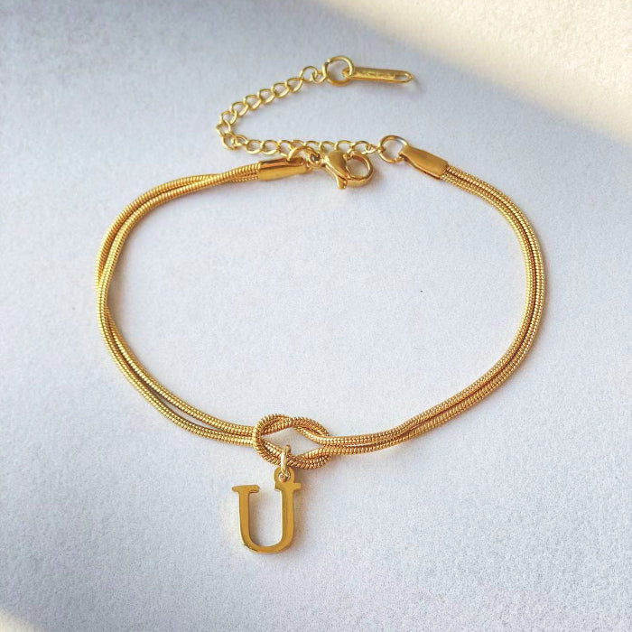 Gold bracelet with a 'U' charm on a light gray background