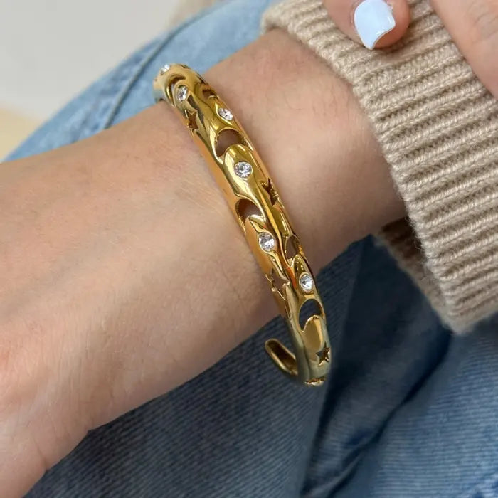 Gold plated celestial bangle with moon and star design, worn on a wrist, perfect for modern jewelry enthusiasts.