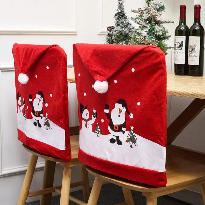 Red Christmas chair covers with Santa and snowman on chairs beside table with wine bottles and mini trees.