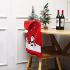 Festive red chair cover with Santa and snowman beside a wooden table decorated with mini Christmas trees.