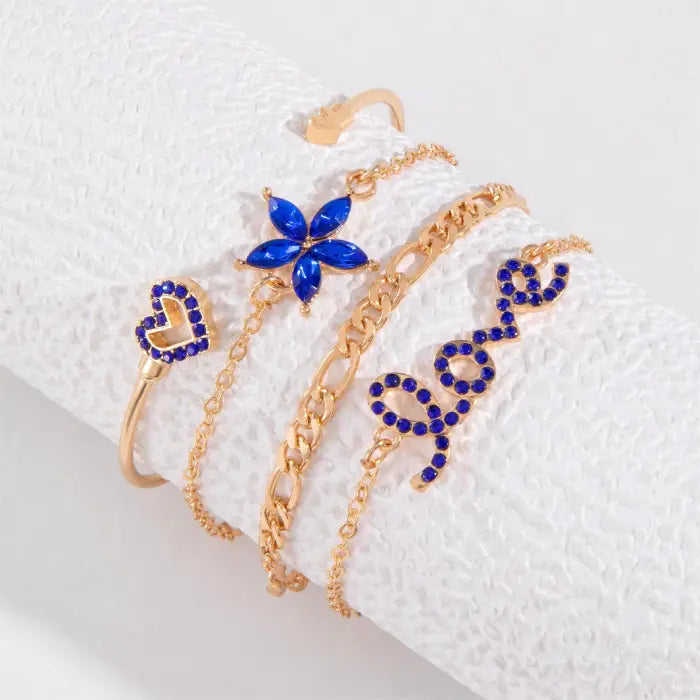 Chic gold bracelet set with “love” script, flower, heart, and chain designs accented by blue gemstones.