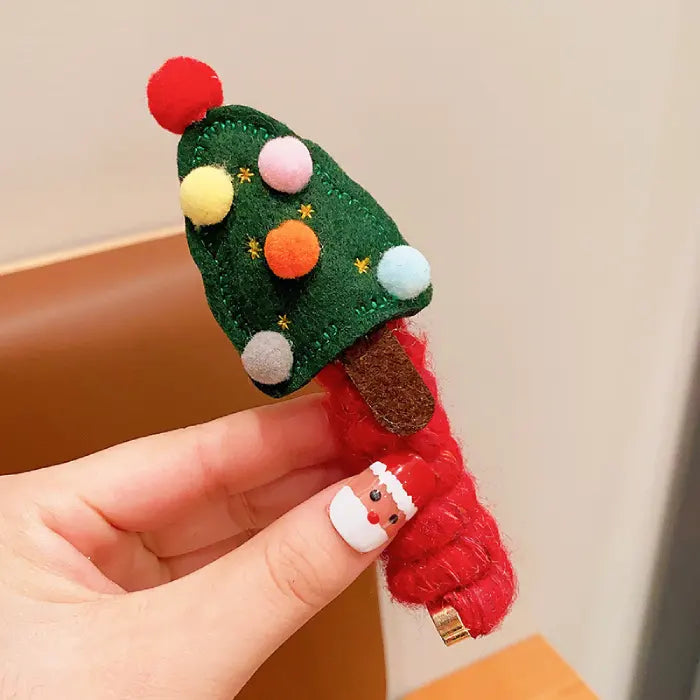 Hand holding a set of Christmas hair ropes with tree and reindeer designs in red, green, and gold accents.