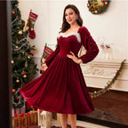 Christmas red velvet dress with white trim worn by a woman posing beside a decorated holiday tree.