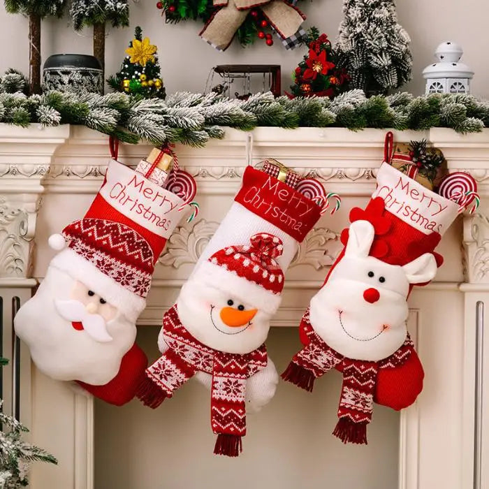 Three festive Christmas stockings featuring Santa, snowman, and reindeer characters hanging on white fireplace mantel with decorative greenery