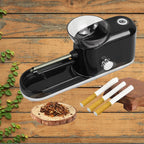 Cigarette Rolling Machine in black placed on wood with loose tobacco and three finished cigarettes.
