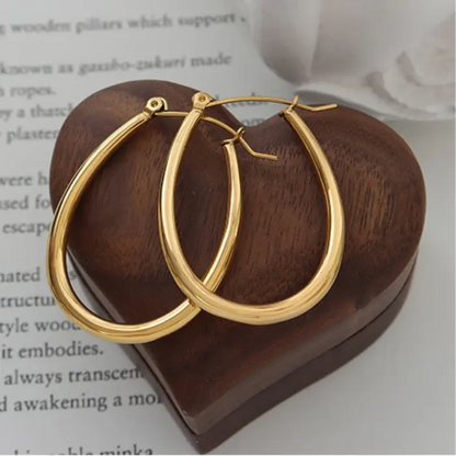 Gold oval hoop earrings displayed on dark wooden heart-shaped surface