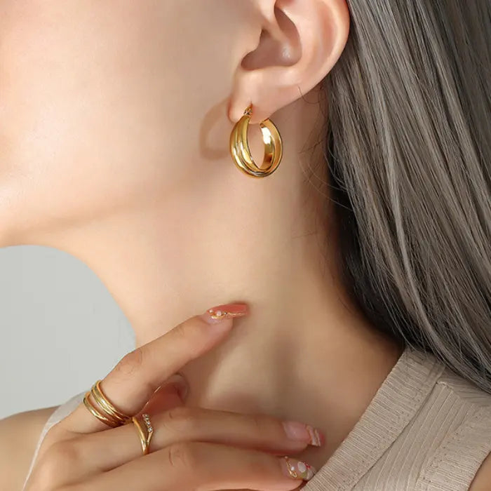 Elegant golden hoop earring shown on ear with coordinating gold rings and neutral outfit