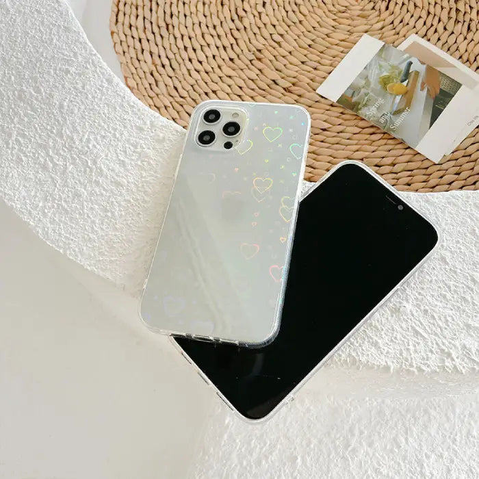 Clear phone case with holographic heart design placed next to a phone, ideal for chic phone protection.