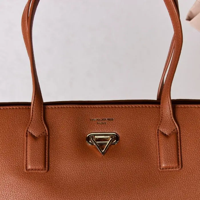 Close-up of brown leather tote bag, focusing on gold hardware, stitching details, and brand logo