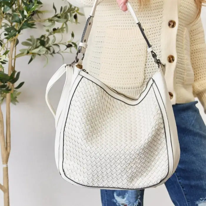 Detailed view of a fashionable white textured handbag with silver hardware, held by woman.