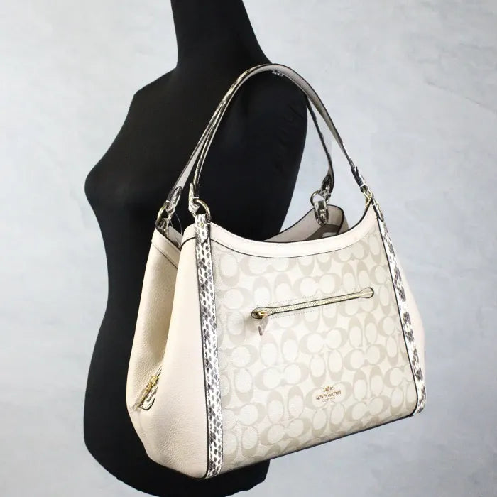 Coach monogram tote bag displayed on mannequin, featuring beige leather and snake print trim.