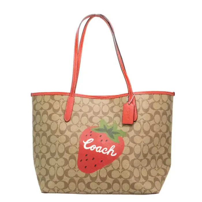 Coach tote bag with strawberry design and monogram print, featuring red handles and logo detail.