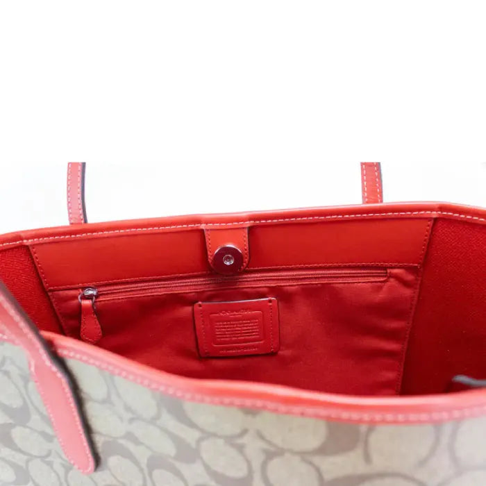 Interior of Coach tote bag with red lining, zip pocket, and branded tag detail.