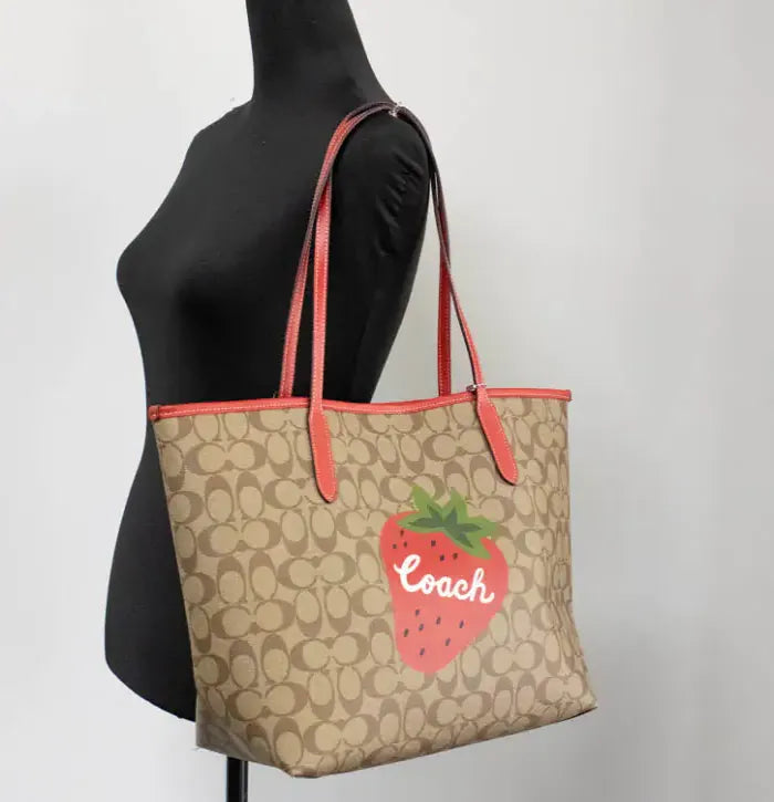 Coach tote bag with strawberry graphic on mannequin, showcasing red leather accents.