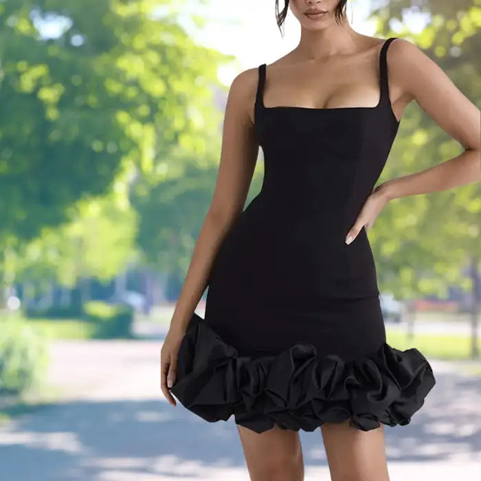 cocktail dress in fitted black design showing detailed square neckline and textured ruffle bottom photographed against natural green park setting