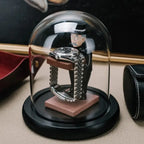 collector watch display dome with a gentleman figurine holding a watch platform, enclosed in a glass dome on a black base.