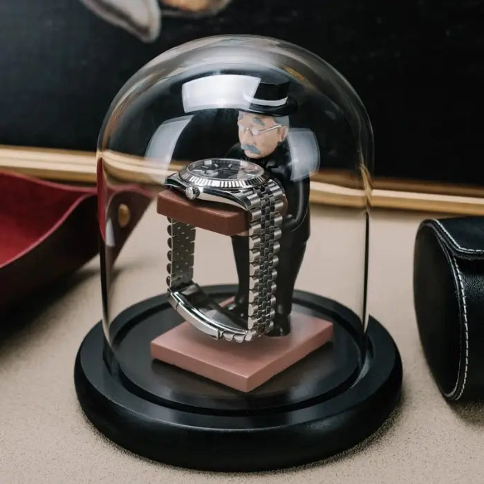 collector watch display dome with a gentleman figurine holding a watch platform, enclosed in a glass dome on a black base.