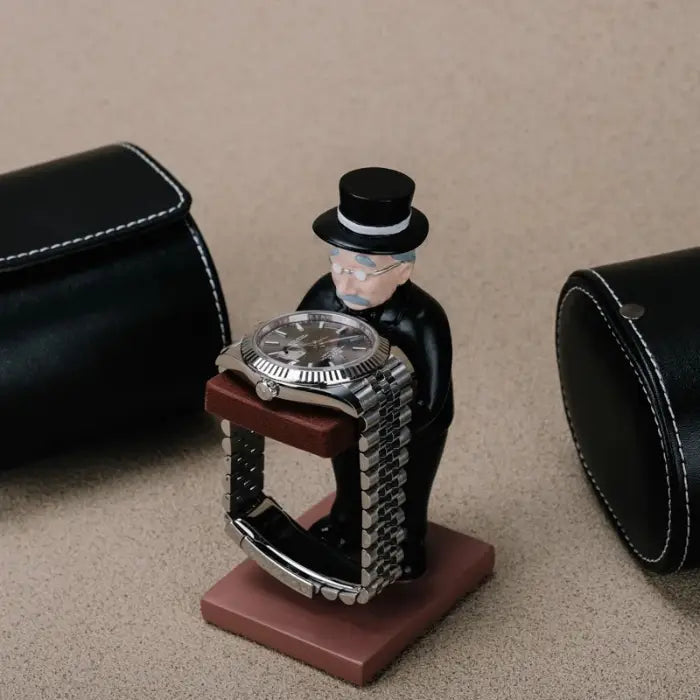 collector watch display with a gentleman figurine holding a watch, surrounded by black leather watch cases on a beige surface.