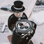 collector watch display featuring a gentleman figurine holding a luxury watch, placed on a table with newspapers in the background.