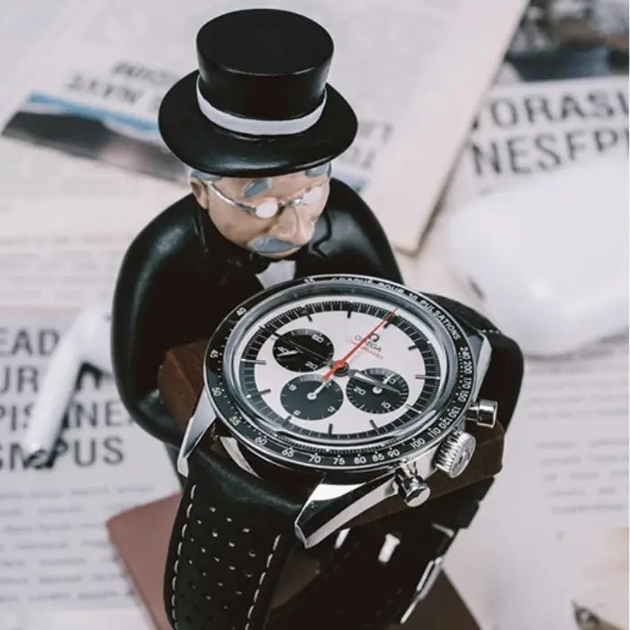 collector watch display featuring a gentleman figurine holding a luxury watch, placed on a table with newspapers in the background.