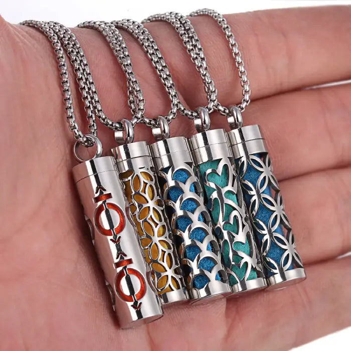 Set of colorful titanium steel aromatherapy pendants displayed on hand with intricate designs.